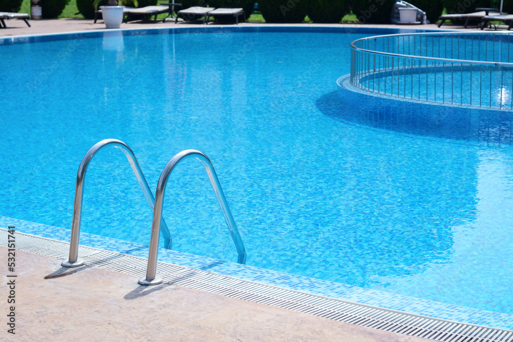 Outdoor swimming pool with ladder and handrails on sunny day, space for text