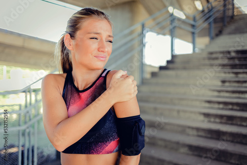 One young caucasian woman holding her sore shoulder while exercising outdoors. Female athlete suffering with painful arm injury from fractured joint and inflamed muscles during workout.