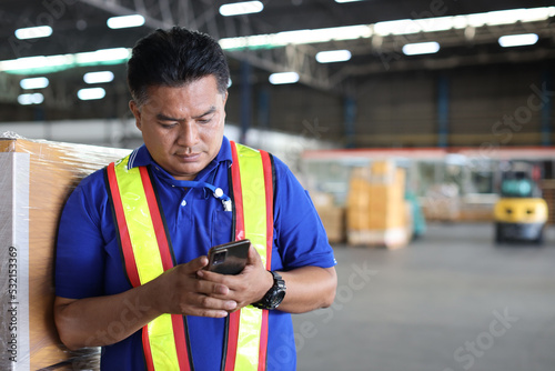 Warehouse workers man with hardhats and reflective jackets using smart mobile phone, walkie talkie radio controlling stock and inventory in retail warehouse logistics, distribution center