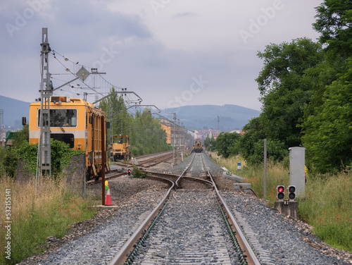 Railway machines on the rails parked on the service tracks waiting to work next to illuminated red signals in a work zone and temporary low tracks at the entrance to Monforte station