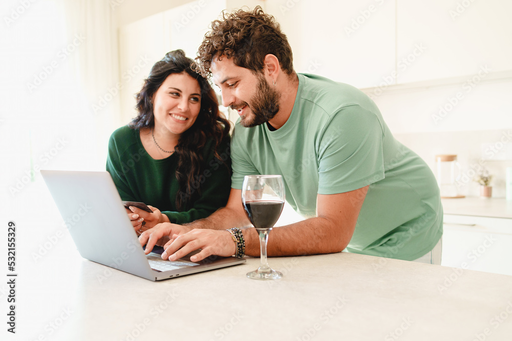 Obraz premium Romantic couple of newlyweds using laptop in the kitchen buying online