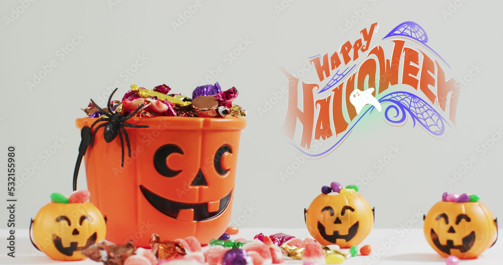 Fototapeta premium Image of halloween text over carved pumpkin bucket with sweets on grey background