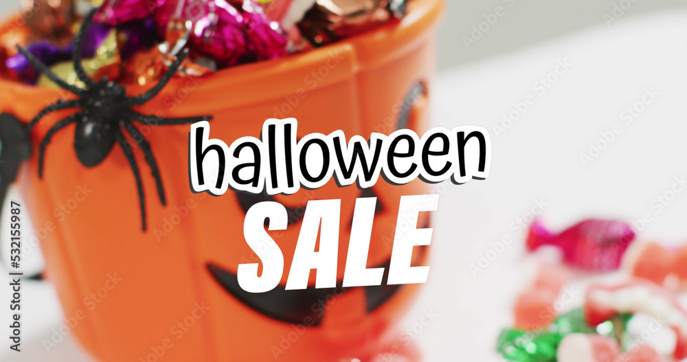 Fototapeta premium Image of halloween sale text over carved pumpkin bucket with sweets on grey background