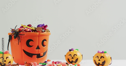 Image of halloween text over carved pumpkin bucket with sweets on grey background