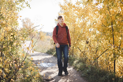 Teenager boy with backpack walking on path in autumn park. Active lifestyle, Back to school. Student boy in fall forest. © Lyubov