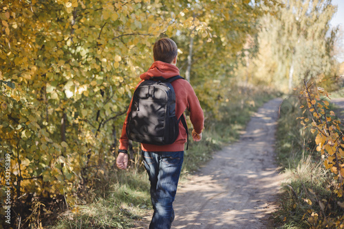 Teenager boy with backpack walking on path in autumn park. Active lifestyle, Back to school. Student boy in fall forest. People from behind