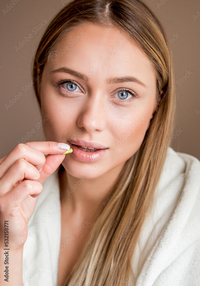 A beautiful happy girl is holding a pill in her hands. A woman in home clothes is sick and being treated. A sick woman with fever and runny nose. Treatment at home with tablets. The girl drinks pills A beautiful happy girl is holding a pill in her hands. A woman in home clothes is sick and being treated. A sick woman with fever and runny nose. Treatment at home with tablets. The girl drinks pills