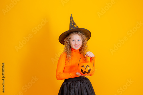 teenage girl in a witch costume on a yellow background  holding a confent pumpkin eating marmalade worms halloween party
