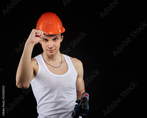 a young construction worker is a teenager in a hard hat and a white T-shirt with a screwdriver in his hand. © justoomm