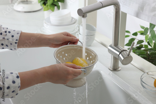 Woman washing fresh ripe lemons under tap water in kitchen, closeup