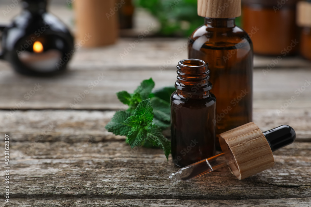 Bottles of mint essential oil and fresh leaves on wooden table, closeup. Space for text