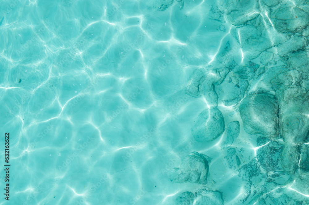 Water background, turquoise shallow sea water. Beautiful texture of sun glare on the water.