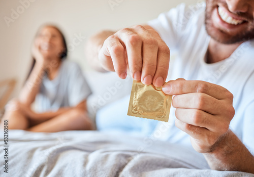 Condom, sex and safety for sexual couple in bed together happy, smile and use protection. Happiness, love and man and woman open birth control contraceptive package to protect against std, sti or hiv photo