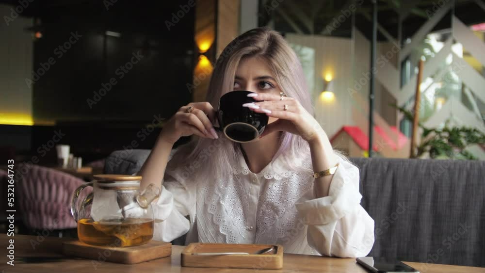 Young blonde business woman sits in a restaurant and drinks tea by the window. Young blonde business woman sits in a restaurant and drinks tea by the window.