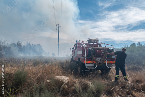 Bombeiros com a sua viatura na luta de um incêndio florestal que vai deixando uma grande nuvem de fumo no ar photo