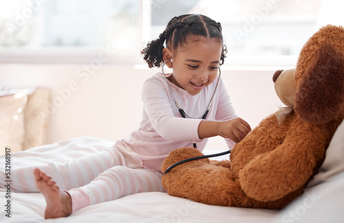 A black girl playing hospital doctor with a teddy bear on her bed, holding a stethoscope and imagining a kid. Child development for a future job as a physician, clinic nurse and medical professional