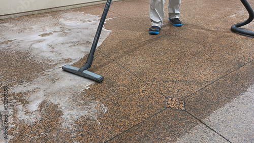 Removal of residual dirty water with a professional vacuum cleaner from a red granite floor