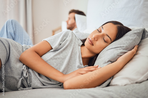 Sleeping, peace and woman asleep on bed with comfortable pillow while taking nap to relax with sleepless partner in background. Couple, sexual problems and carefree wife lying eyes closed next to man photo