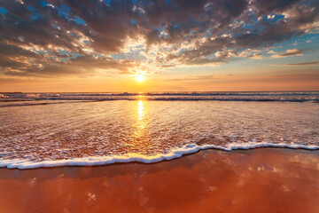 Beautiful sunrise with dramatic cloudscape over the sea waves and beach