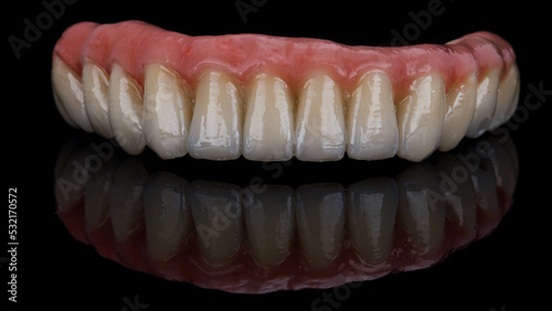 ceramic dental prosthesis with the gums of the lower jaw on black glass with reflection