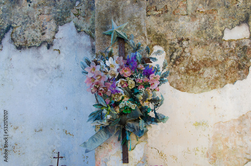 Un mazzo di fiori di metallo sul muro scrostato di una cappella di famiglia nel cimitero di Tricase, borgo del Salento in Puglia