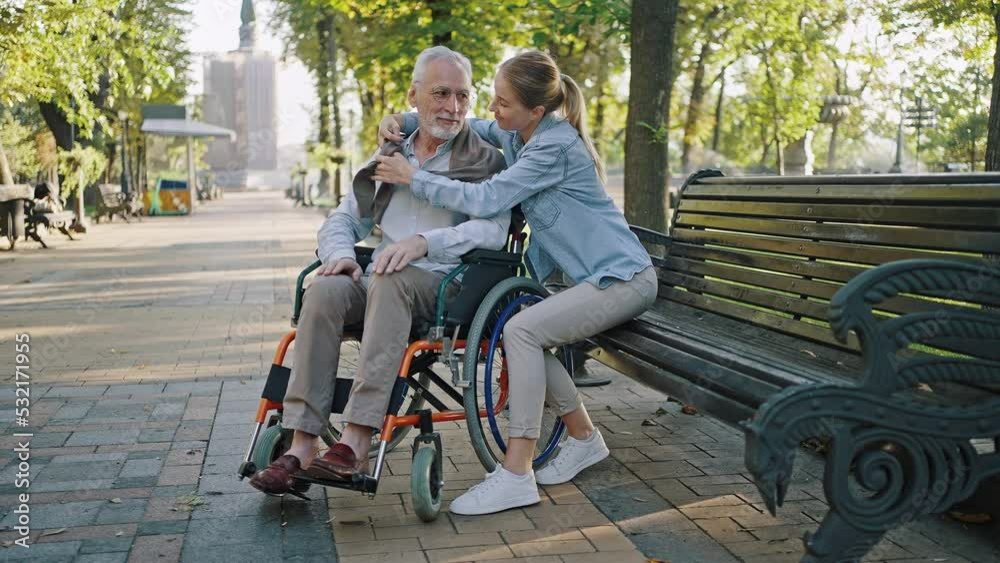 Young woman covers disabled senior father with sweater Young woman covers disabled senior father with sweater