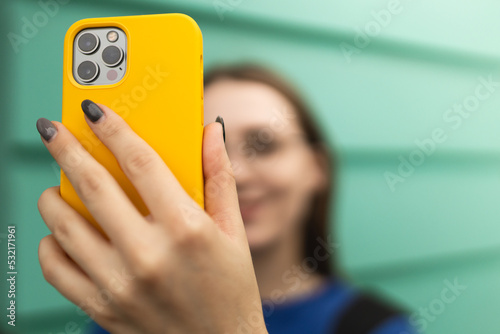 A girl in a blue sweater holds a phone in a yellow case and talks online. Rumov online. Remote communication. A girl walks around the city and takes a selfie.