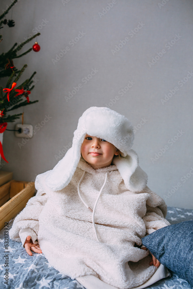 Cute child y on the bed in cozy adult clothes and a hat with earflaps. Cute child y on the bed in cozy adult clothes and a hat with earflaps.