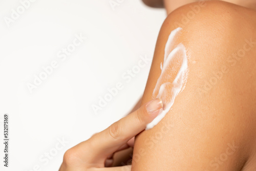 Close up young woman smearing shoulder with cream