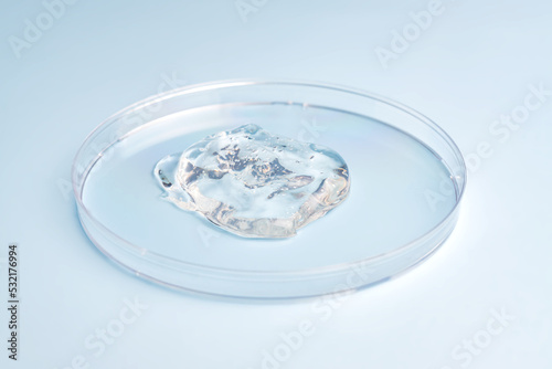 Petri dish with gel or cosmetic liquid on blue background. Transparent container with gel with bubbles. Texture of the gel. Medicine and beauty concept. Medical glassware for laboratories