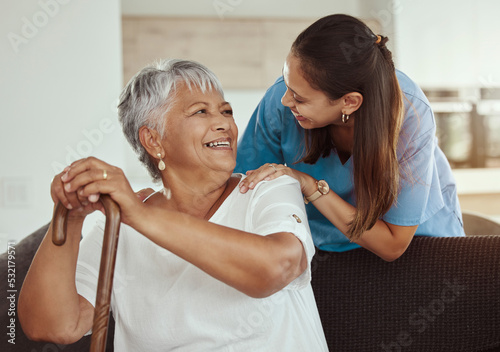 Happy, relax and senior woman with caregiver smile while sitting on a living room sofa in a nursing home. Support, help and professional nurse or healthcare worker helping elderly lady or patient