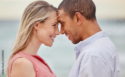 Portrait of couple at the beach with their forehead touching. Multiracial man and woman in relationship, happy, smiling and in love on vacation. Bonding, love and quality time together