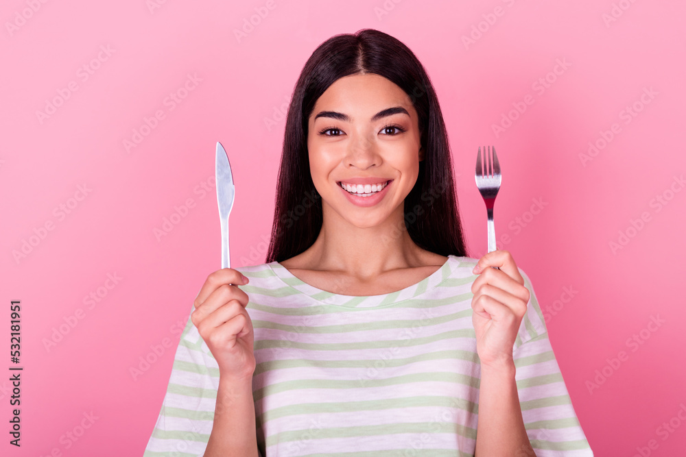 Portrait of nice cheerful person arms hold fork knife toothy smile isolated on pink color background Portrait of nice cheerful person arms hold fork knife toothy smile isolated on pink color background
