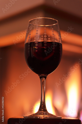 Glass with red wine and the fireplace as background