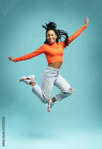 Excited happy pretty girl in casual jeans clothes high jump with raised hands and legs, on blue background.