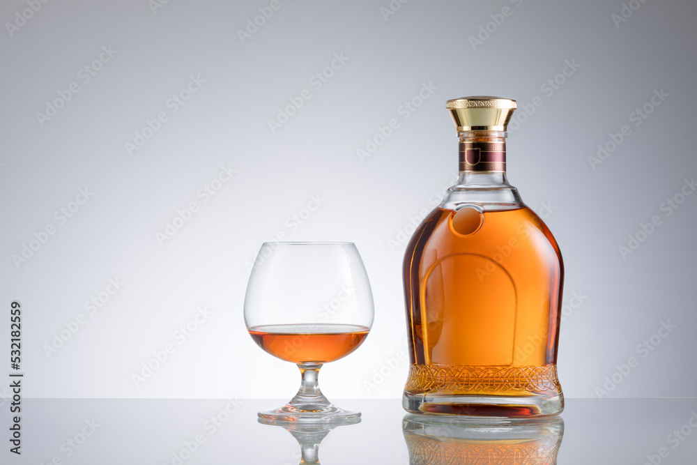 view of glass of cognac and a bottle aside on grey background. view of glass of cognac and a bottle aside on grey background.