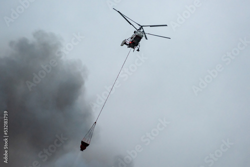 A fire helicopter carries a container of water to extinguish a fire in a production building