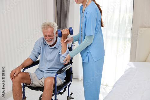 Happy caregiver helping senior elderly man lifting dumbbell and excercise with wheelchair at home or retirement house. Asian smiling nurse taking good help care and support of elder patient at house.