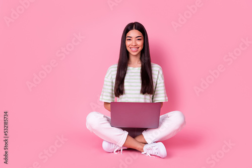Full body photo of cheerful malaysian lady sit floor toothy smile use netbook isolated on pink color background