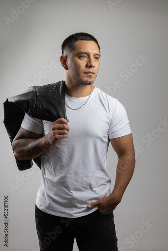 young male model wearing white t-shirt, necklace and holding black leather jacket, urban and casual fashion, latin man posing, lifestyle