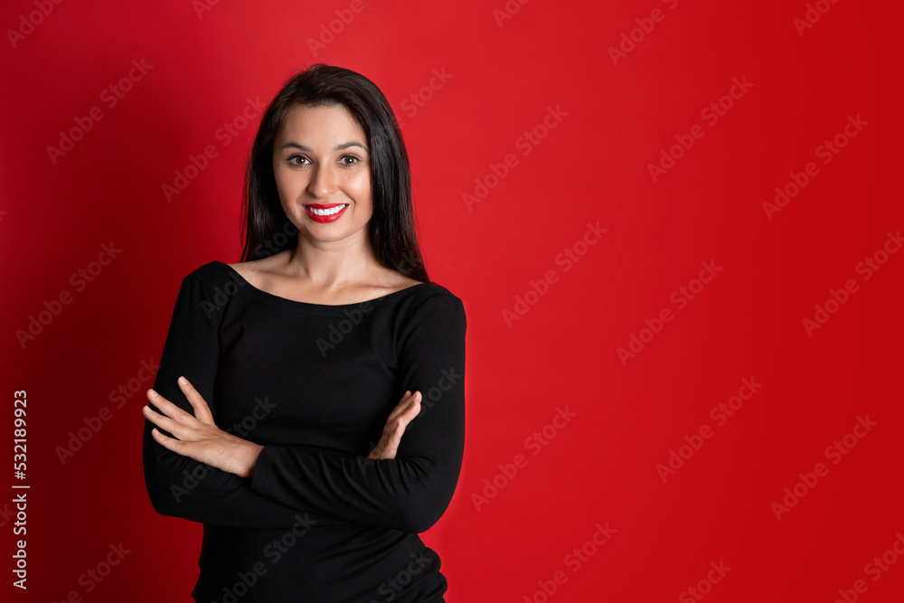 Studio Portrait of a Beautiful Young Woman in a Black Dress with Red Lipstick on Her Lips. Red colored background. Studio Portrait of a Beautiful Young Woman in a Black Dress with Red Lipstick on Her Lips. Red colored background.