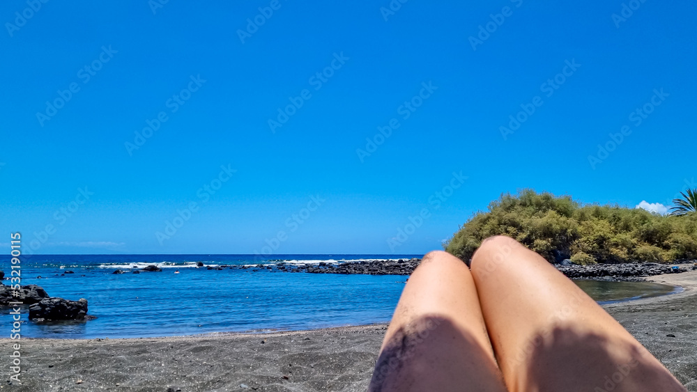 Sunbathing and relaxing woman on beach in Valle Gran Rey, La Gomera, Canary Islands, Spain, Europe. Female feet and legs on the beach under the sun. Recreation, relaxation, vacation summer concept. Sunbathing and relaxing woman on beach in Valle Gran Rey, La Gomera, Canary Islands, Spain, Europe. Female feet and legs on the beach under the sun. Recreation, relaxation, vacation summer concept.