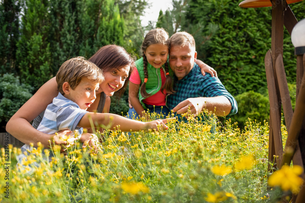Obraz premium Happy family in garden looking at plants on sunny day