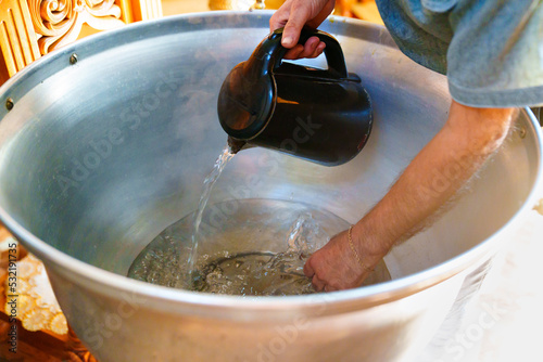 woman pours warm water from a kettle into a baptismal font in an Orthodox church