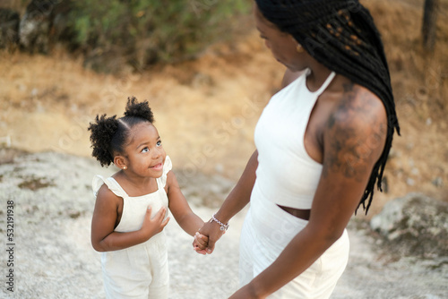 Crop black woman with cute little daughter holding hand in nature photo