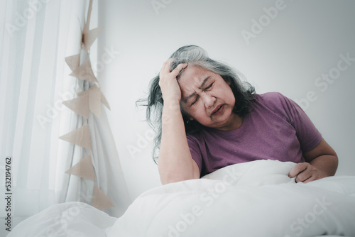 Unhealthy elderly senior Asian woman sitting on bed suffering from headache and migraine so pain and illness, Stress senior woman sit on bed at home alone, tried, Unhappy Elderly despond concept