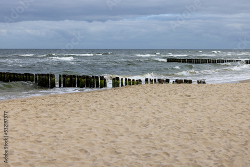 Fototapeta Naklejka Na Ścianę i Meble -  Seaside landscape, foamy water of the Baltic Sea with a wooden breakwater. Cloudy sky, Island Wolin, Miedzyzdroje, Poland