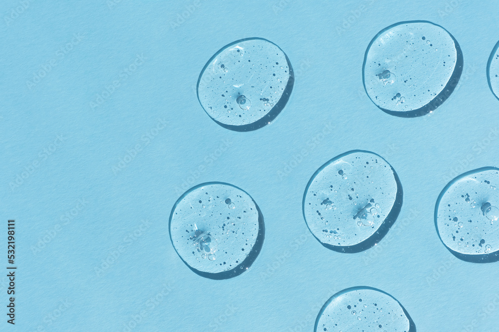 Naklejka premium Drops of serum or hyaluronic acid gel on a blue background. Smears of cosmetic skin care products. Wellness and beauty concept.