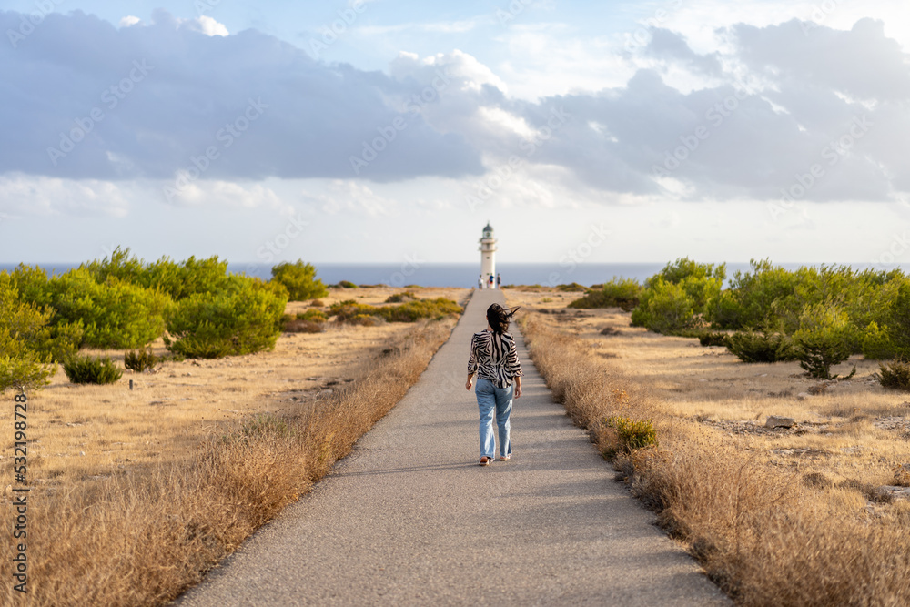 Obraz premium Young woman walks to a lighthouse in sunset