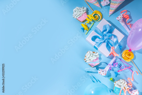 Happy birthday greeting card background. Flatlay with colorful holiday tools - birthday party caps, blowers, gift boxes , balloons, steamers, candles, on blue background copy space